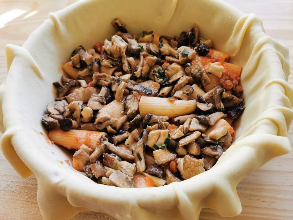 Sautéed mushrooms in a layer on top of pasta and ragu inside pie.