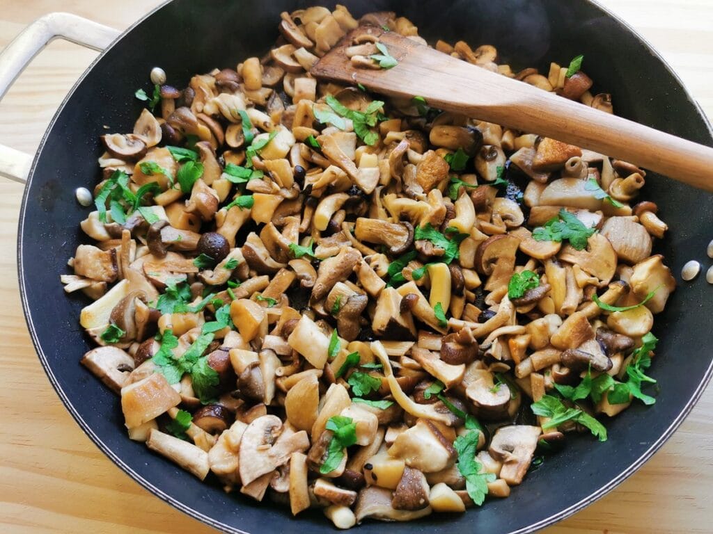 mixed mushrooms cooking in skillet with chopped parsley