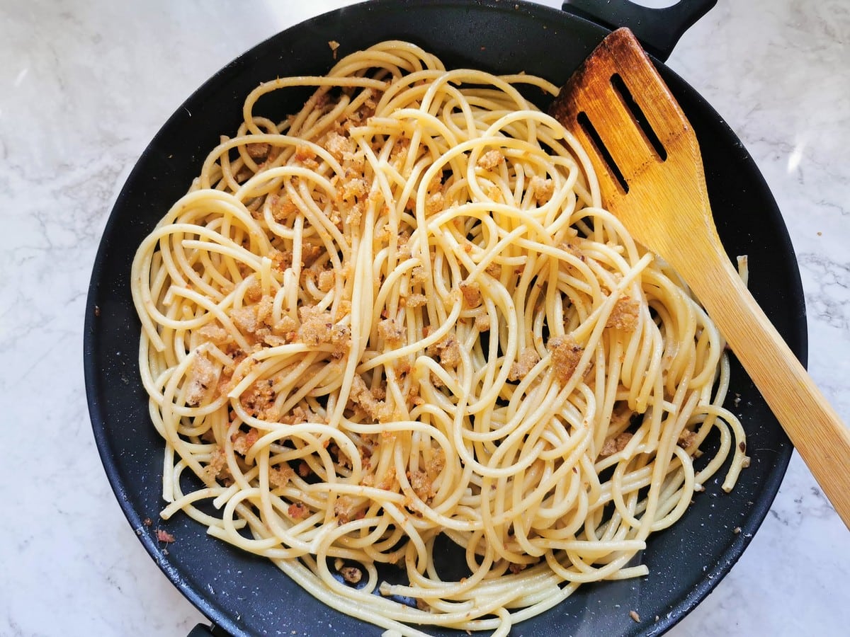 Cooked bucatini in skillet with breadcrumbs and anchovies.