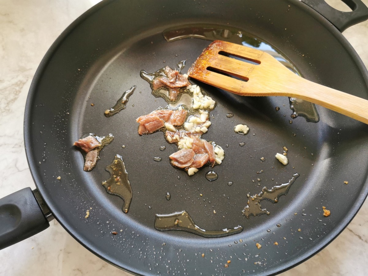 Pieces of anchovies and chopped garlic in skillet with olive oil.