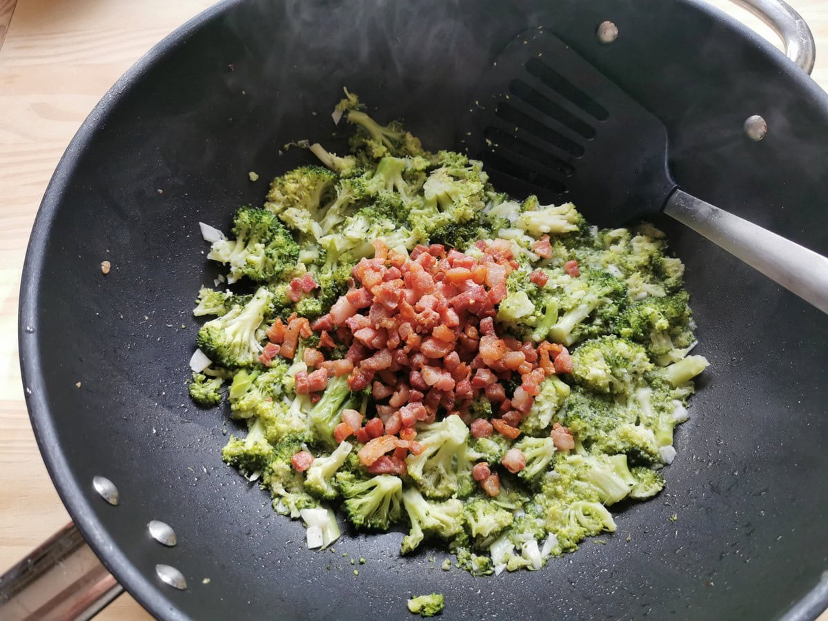 Cooked pancetta cubes in frying pan with cooked broccoli florets.
