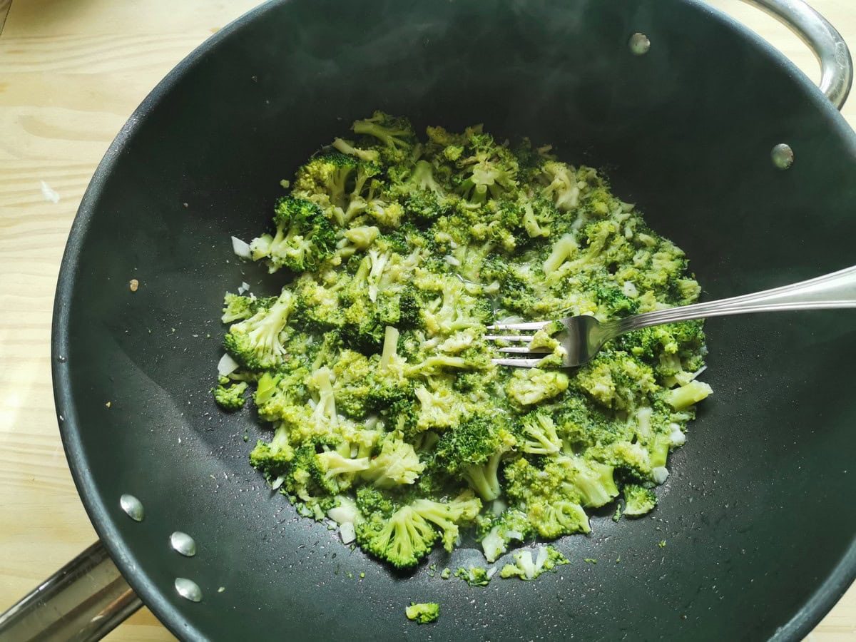 Broccoli florets in pan with chopped garlic and a fork.
