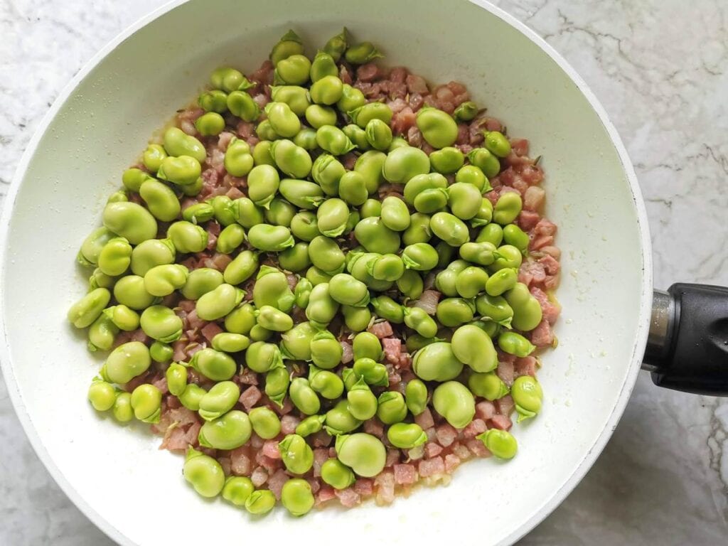 shelled fava beans in pan with cooked pancetta and garlic