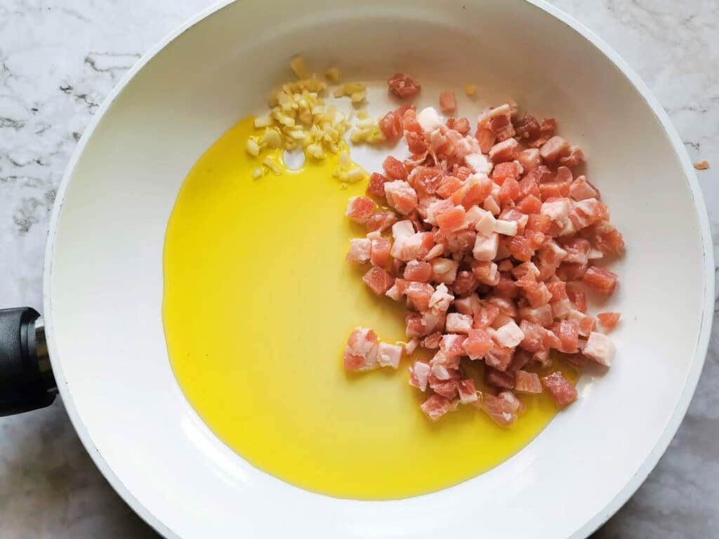 pancetta cubes and chopped garlic cooking in olive oil in pan