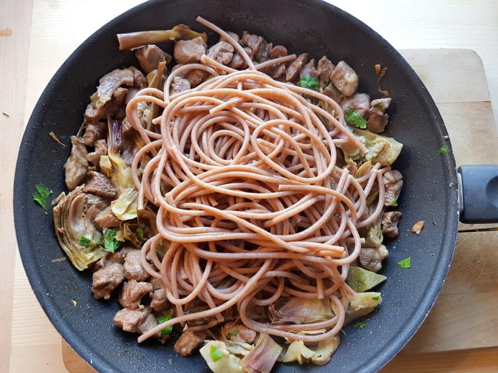 whole-wheat spaghettoni pasta with lamb and artichokes in skillet