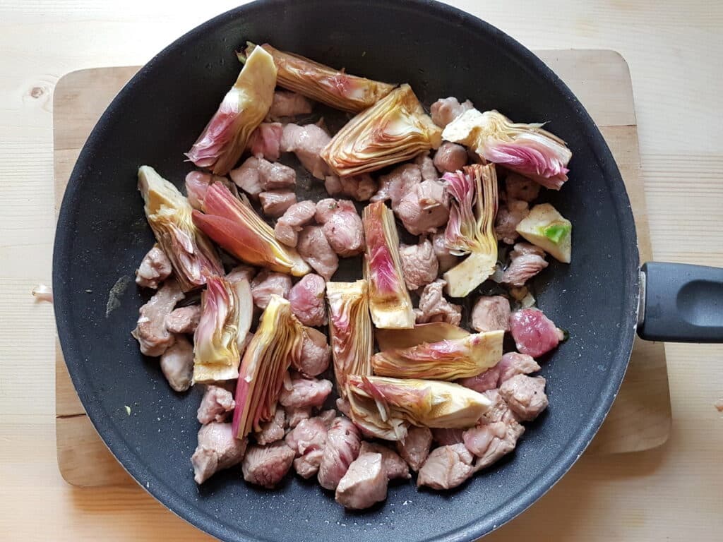 cooked lamb and uncooked artichokes in skillet
