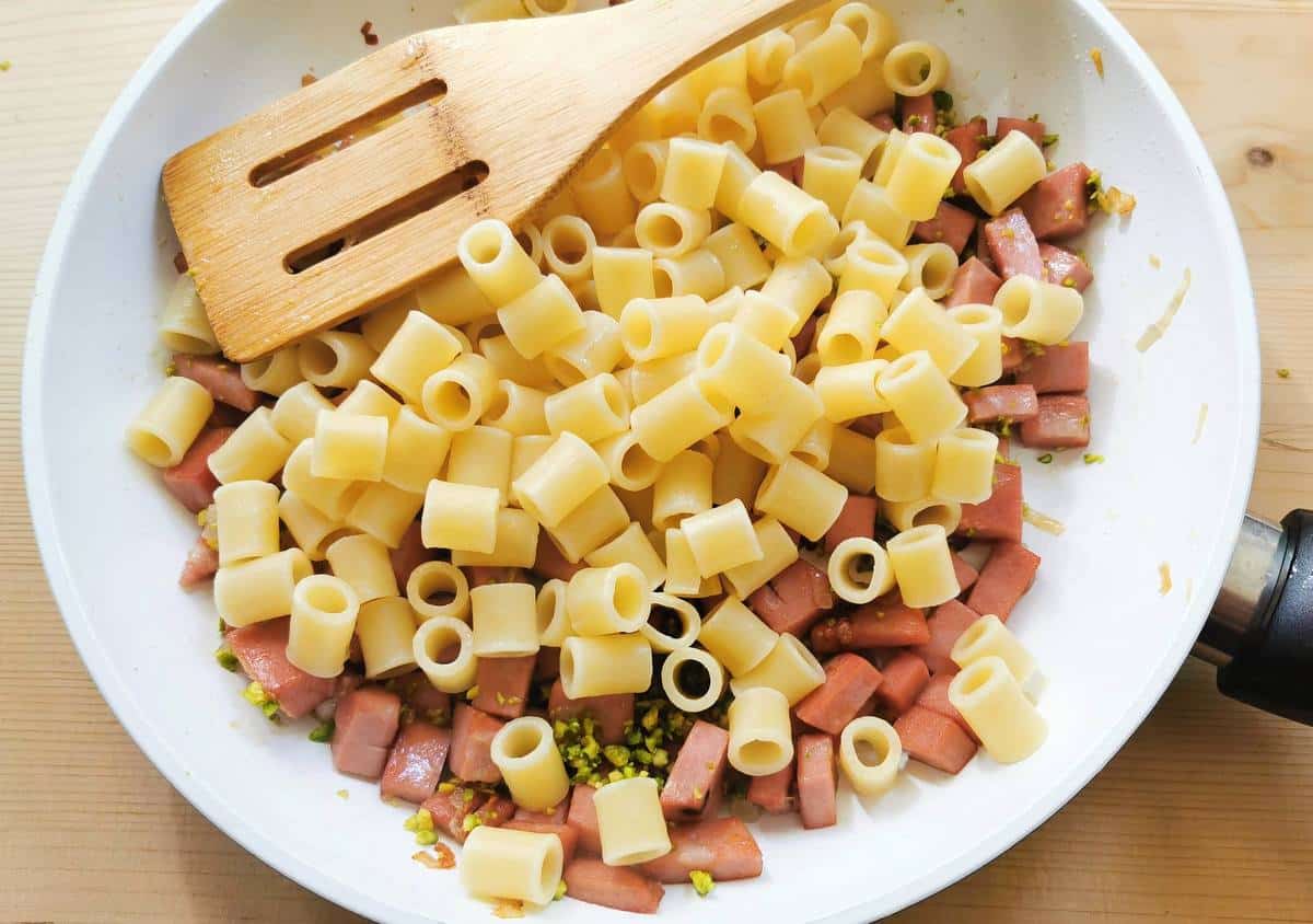 cooked pasta added to mortadella and pistachios in pan