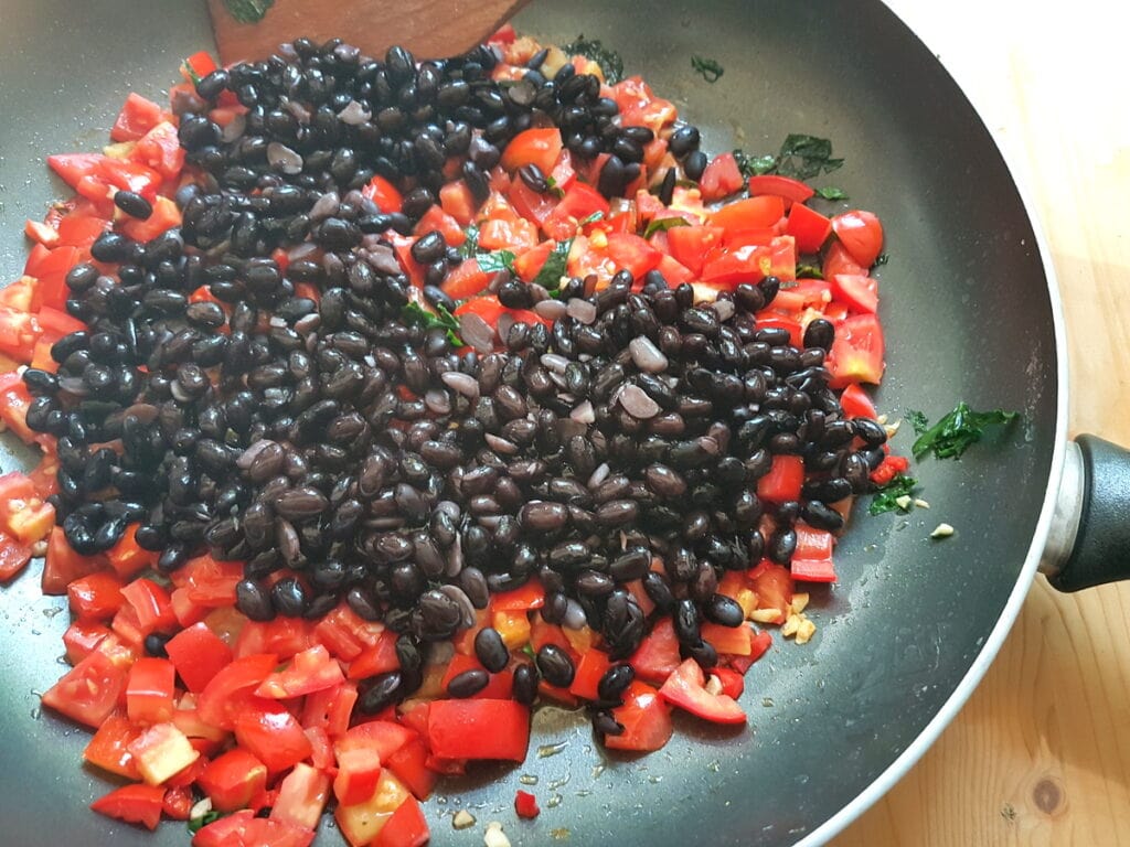 black beans in skillet with tomatoes and other sauce ingredients