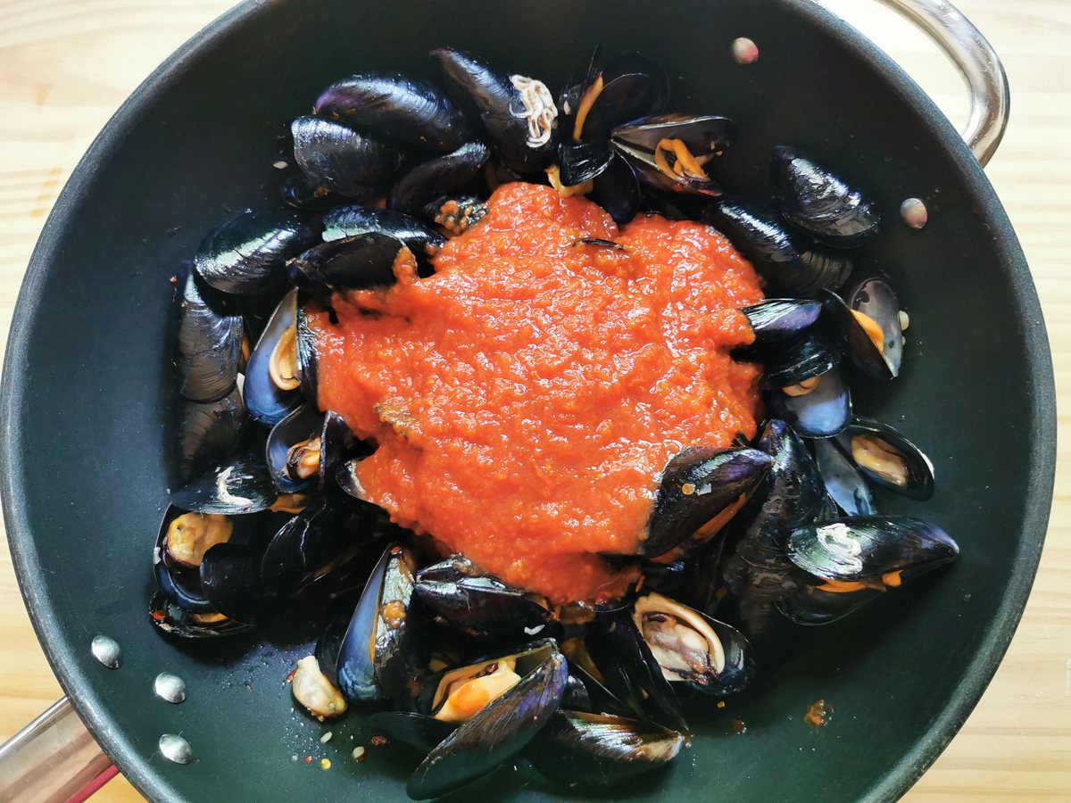 Cooked mussels in large skillet with added tomato passata.