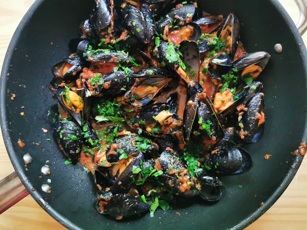 Cooked mussels in tomato sauce with chopped parsley sprinkled on top.