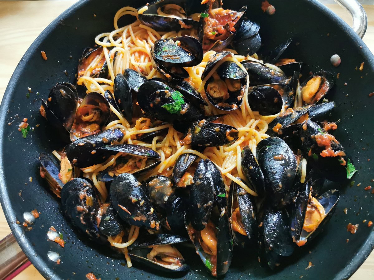 Cooked spaghetti mixed with cooked mussels and tomato sauce in large skillet.