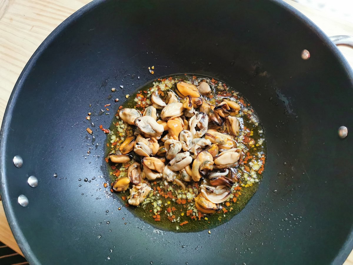 Chopped garlic, red pepper flakes and shelled mussels cooking in olive oil in large skillet.