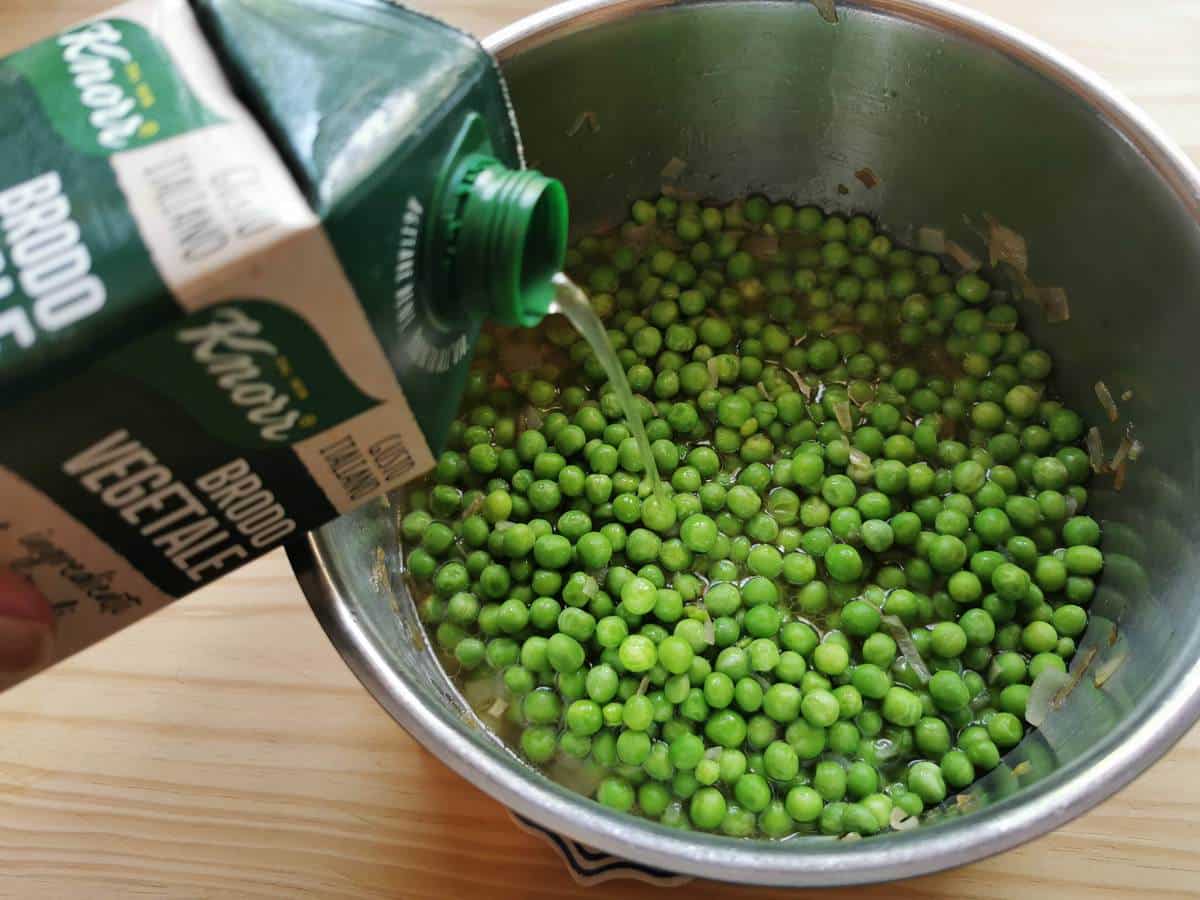 Vegetable broth added to peas and shallots in pan.