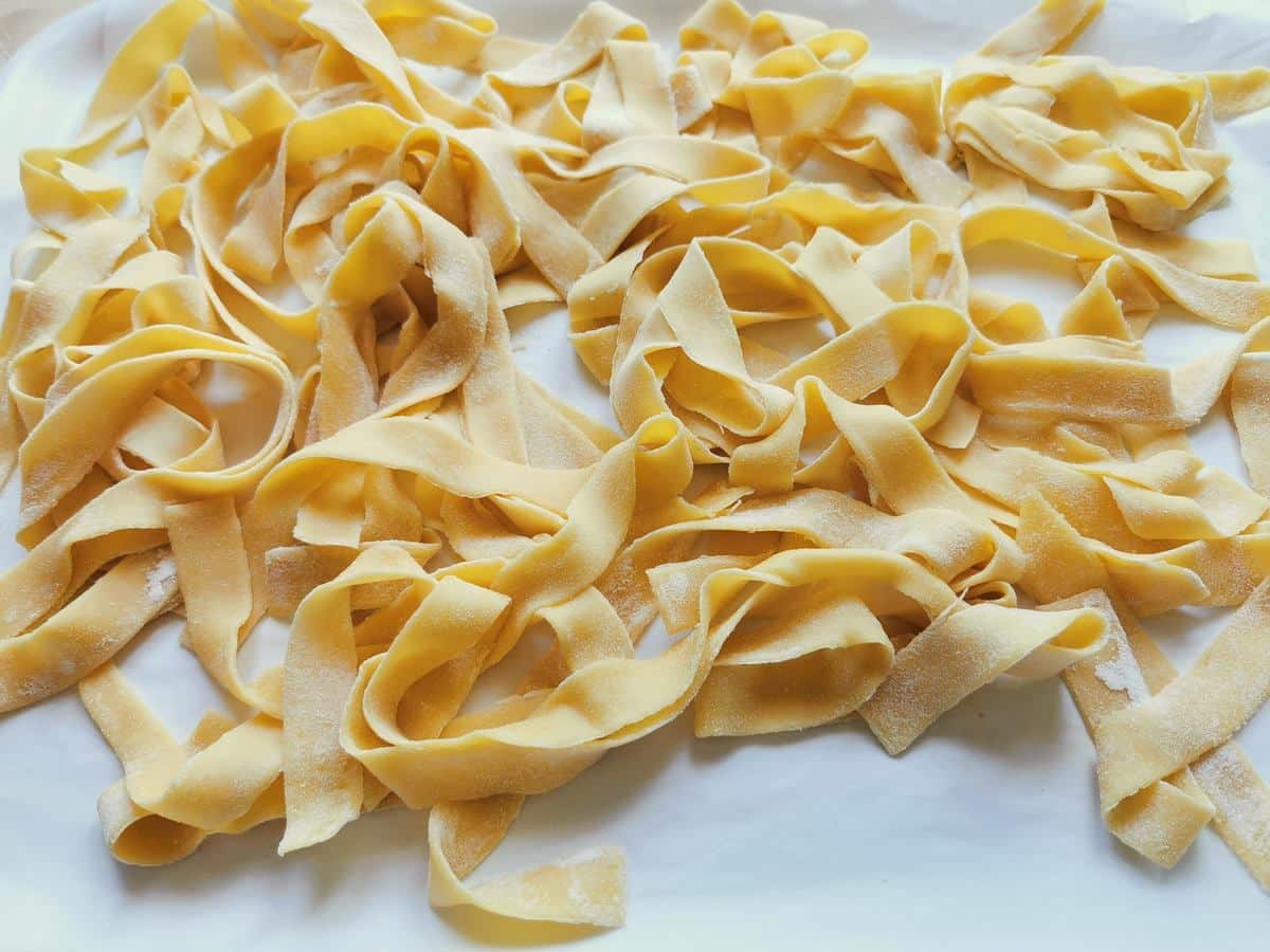 Homemade egg pasta ribbons (pappardelle) on white paper.