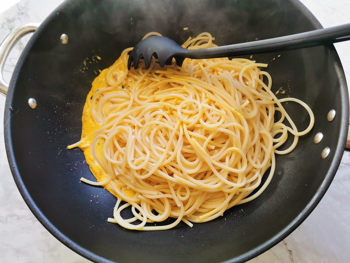 Adding pasta to the pan with the saffron sauce.