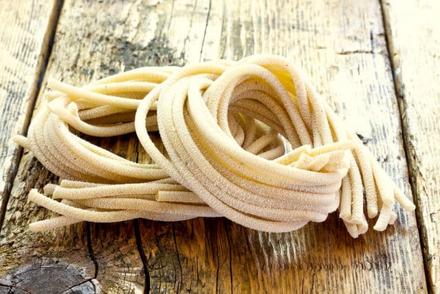 fresh pici pasta nests on wooden table