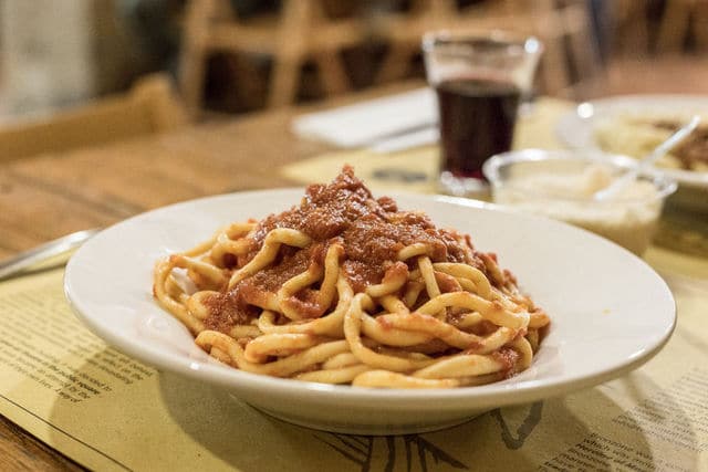 handmade pici pasta with ragu in white bowl