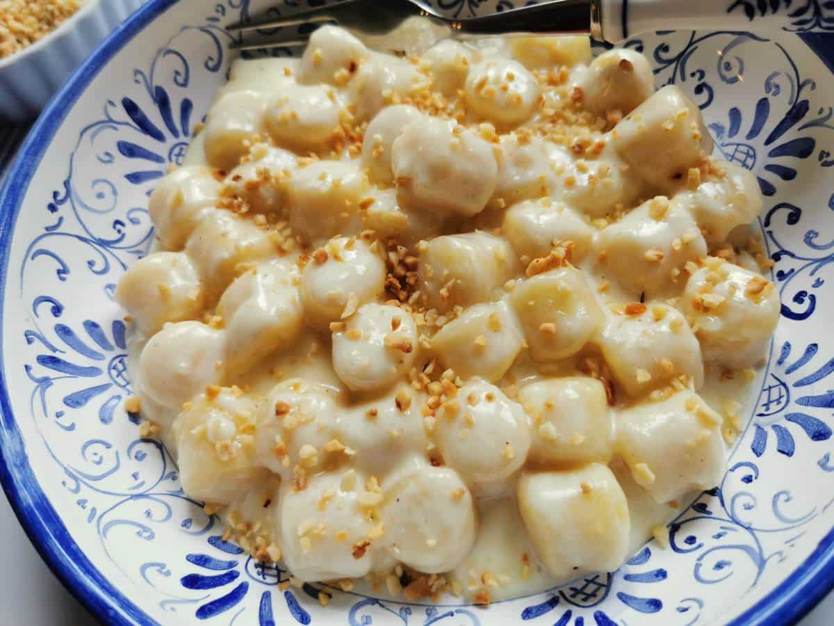 Gnocchi al Castelmagno topped with hazelnut granules in ble and white bowl.