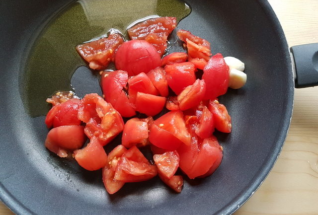 peeled and chopped fresh tomatoes in frying pan with garlic and olive oil