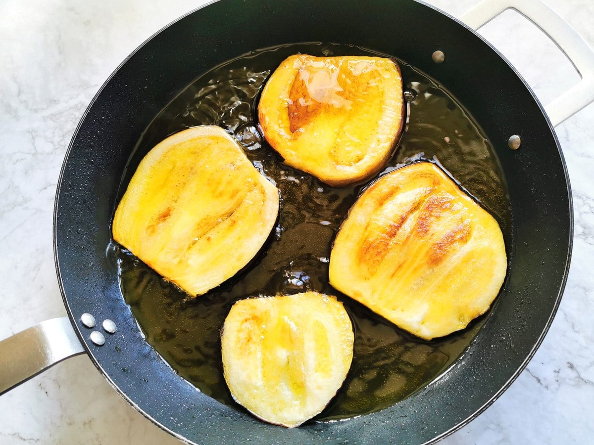 egglant slices cooking in olive oil in  frying pan.