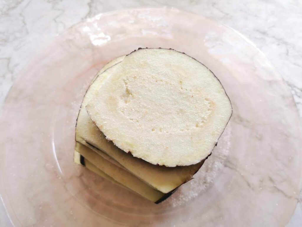 eggplant slices covered in salt on plate.