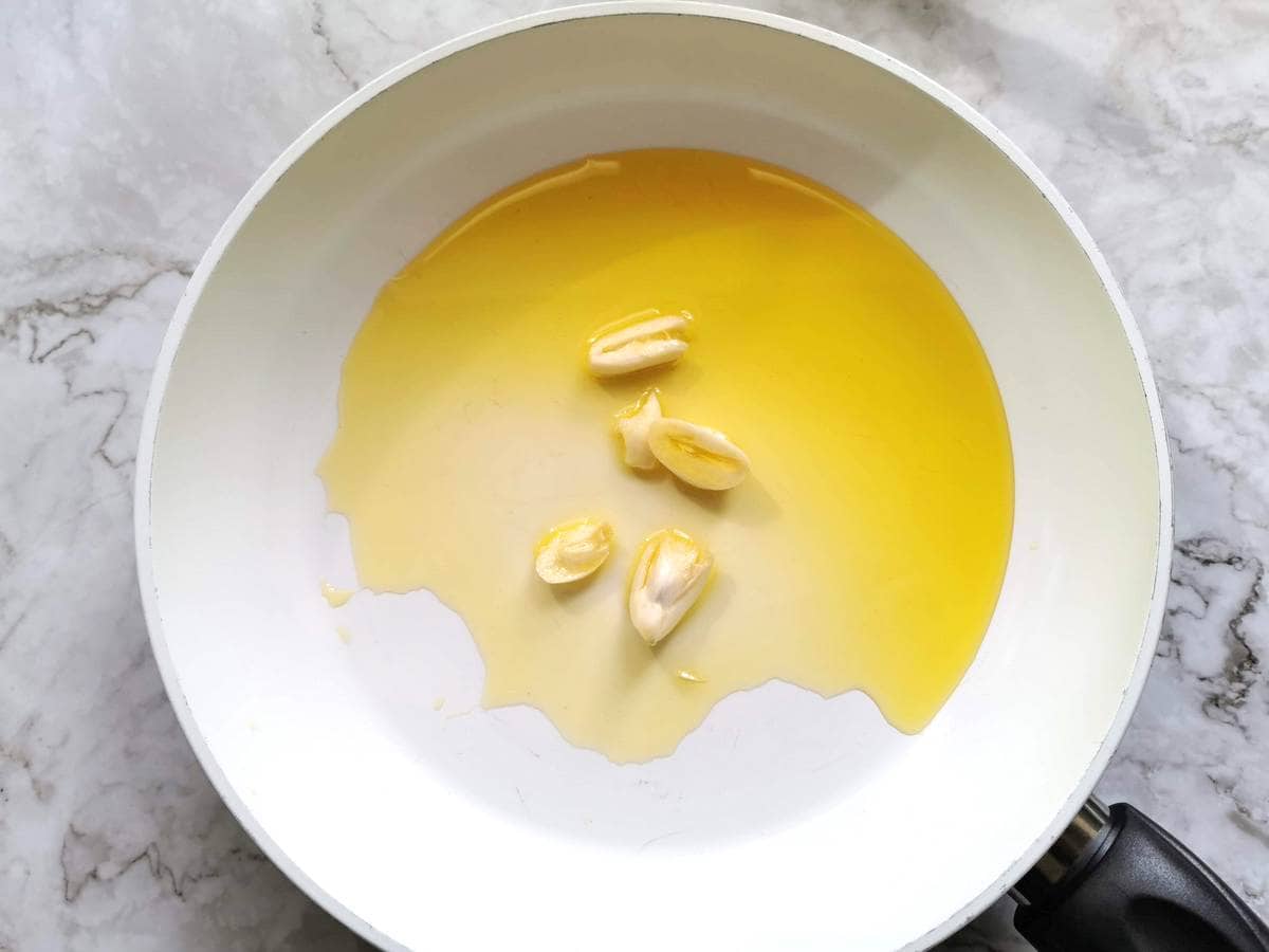 Peeled garlic cloves cooking in olive oil  in frying pan.