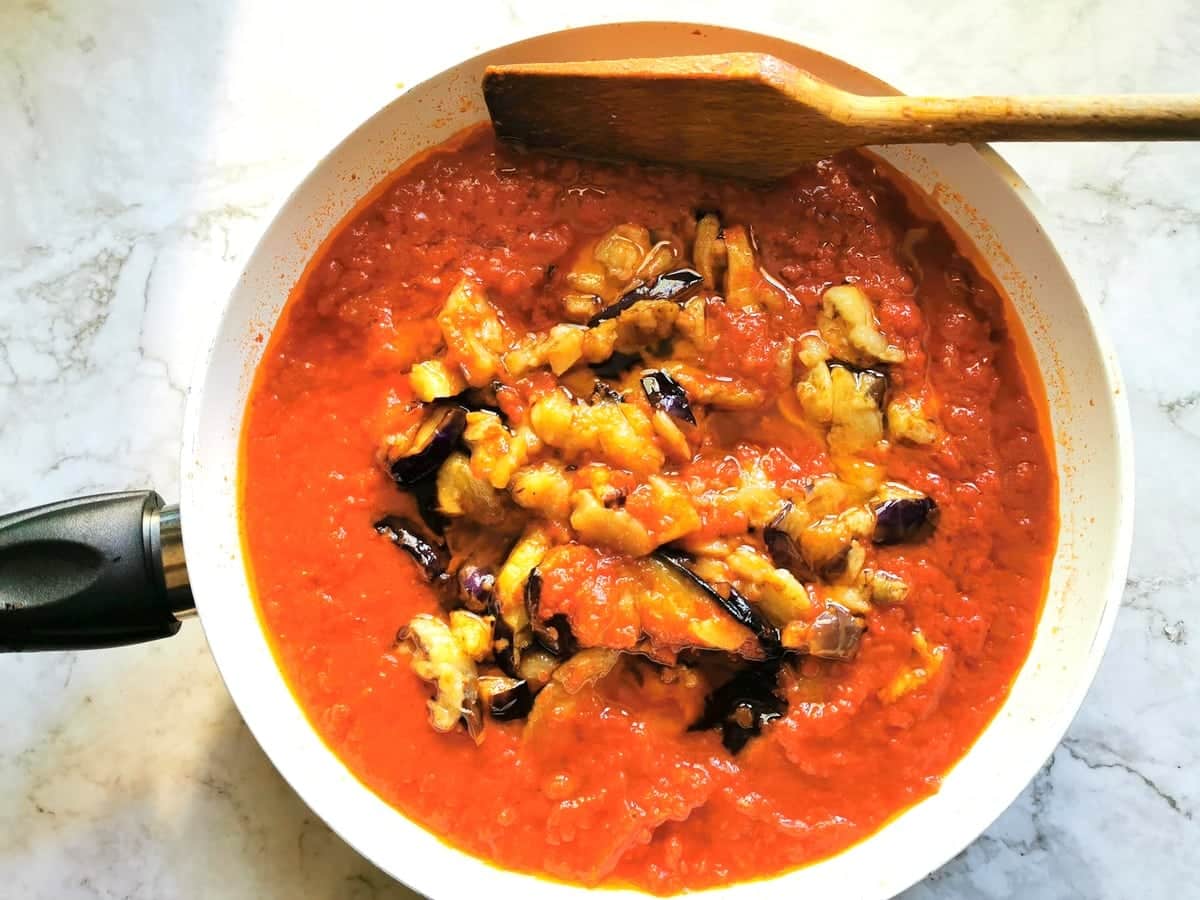 pieces of fried eggplant in frying pan with tomato sauce.