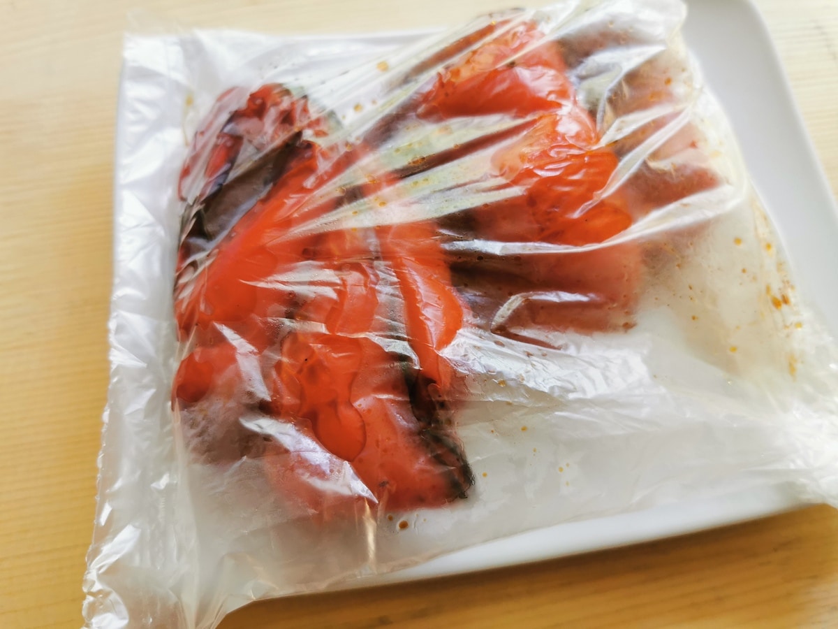 Roasted red peppers steaming in a dish covered in plastic wrap.