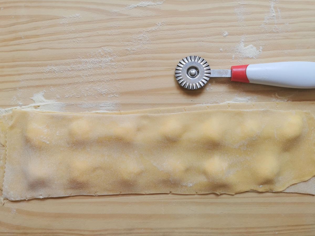 A rolled out ravioli pasta dough sheet on top of a second sheet with robiola cheese filling inbetween.