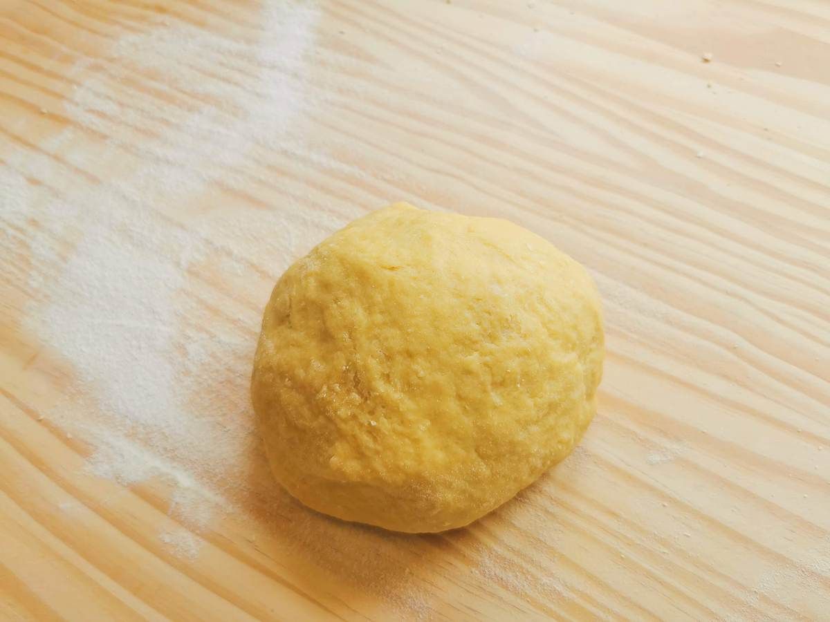 Ready ball of pasta dough on wood work surface.