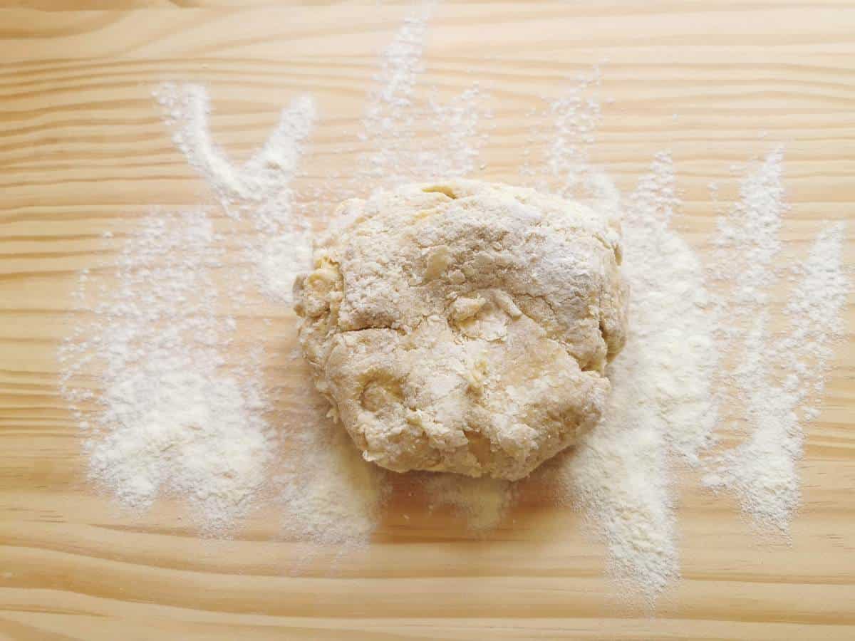 Rough pasta dough ball on flour dusted wood work surface.