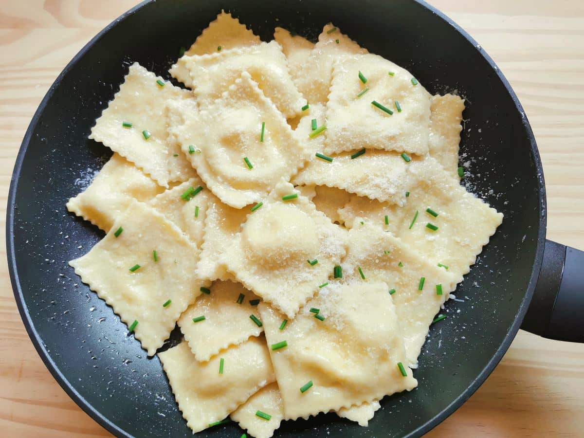 Cooked robiola filled ravioli in skillet with melted butter, grated cheese and chopped chives.