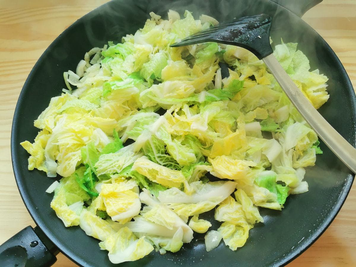 Pre-boiled cabbage slices cooking in frying pan.