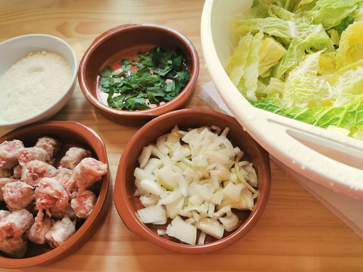 Washed cabbage leaves in colander. Skinned and chopped sausage, peeled and chopped onion and chopped parsley in small terracotta bowls.