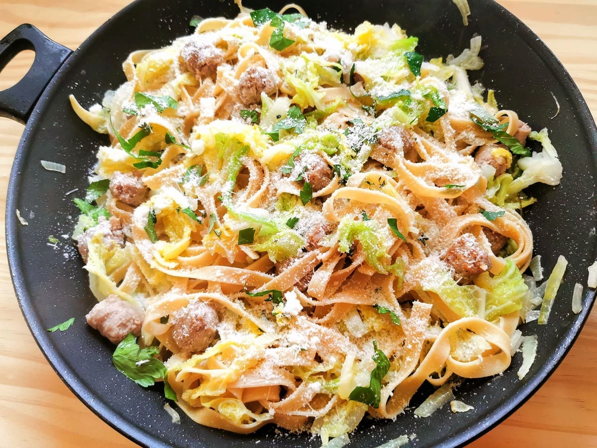 Sausage and cabbage tagliatelle in frying pan with grated parmigiano sprinkled on top.