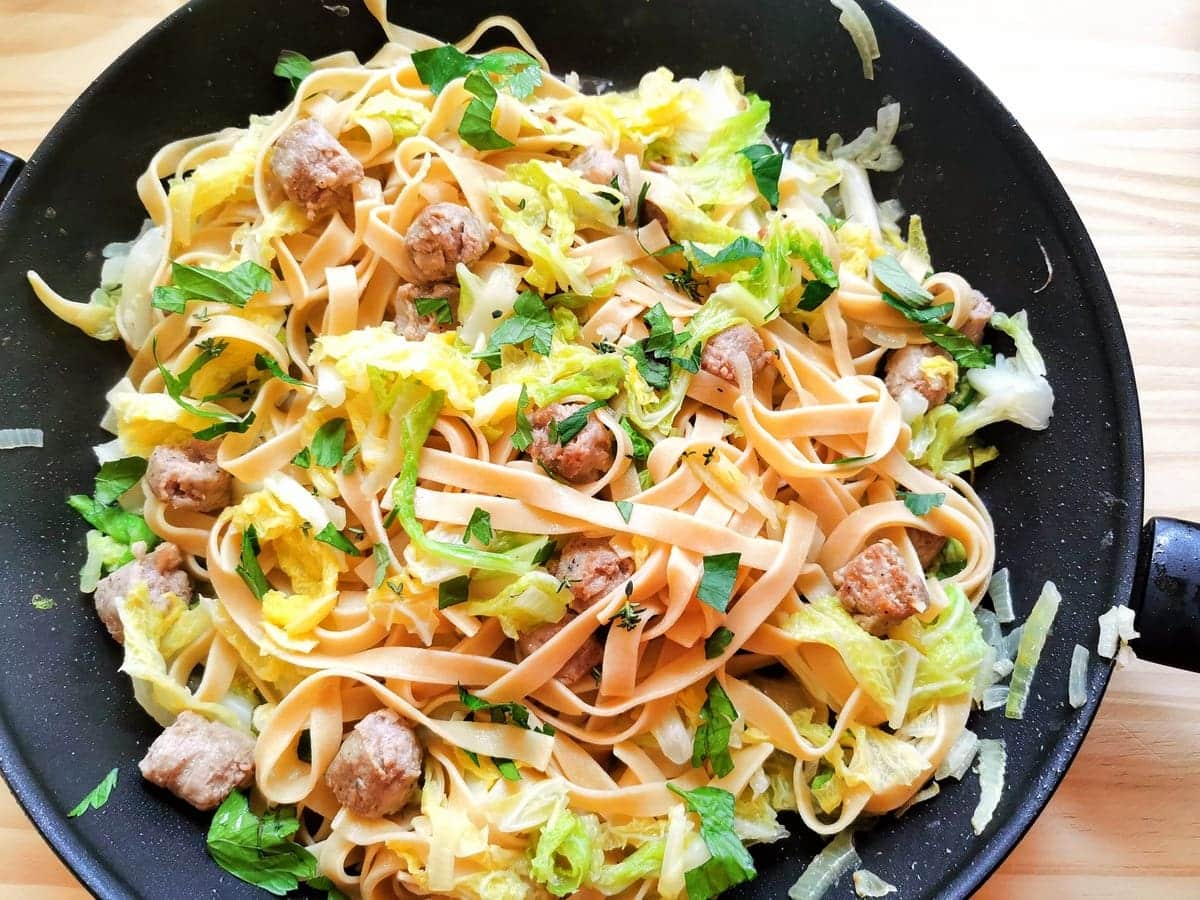 Sausage and cabbage tagliatelle in frying pan with fresh herbs sprinkled on top.