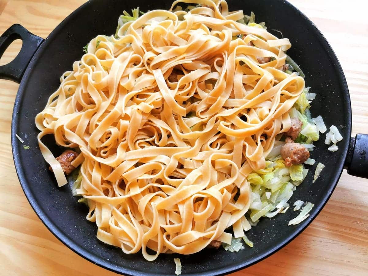 Cooked tagliatelle in pan with sausage and cabbage.