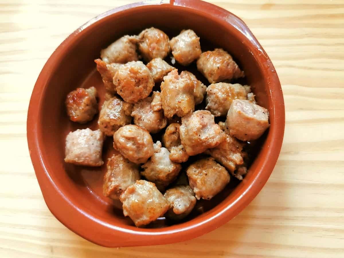 Browned pieces of sausage in small terracotta bowl.