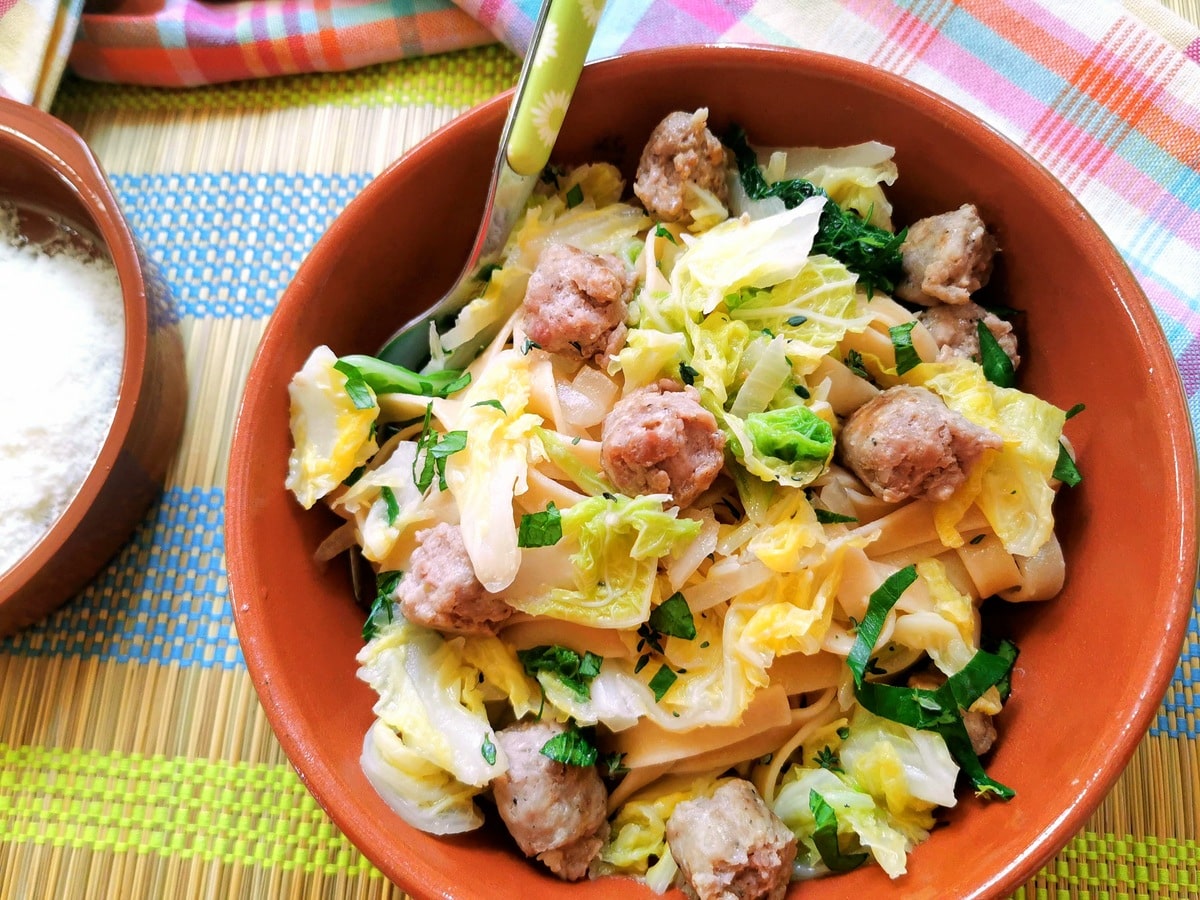 A portion of sausage and cabbage pasta in a terracotta bowl with a fork.