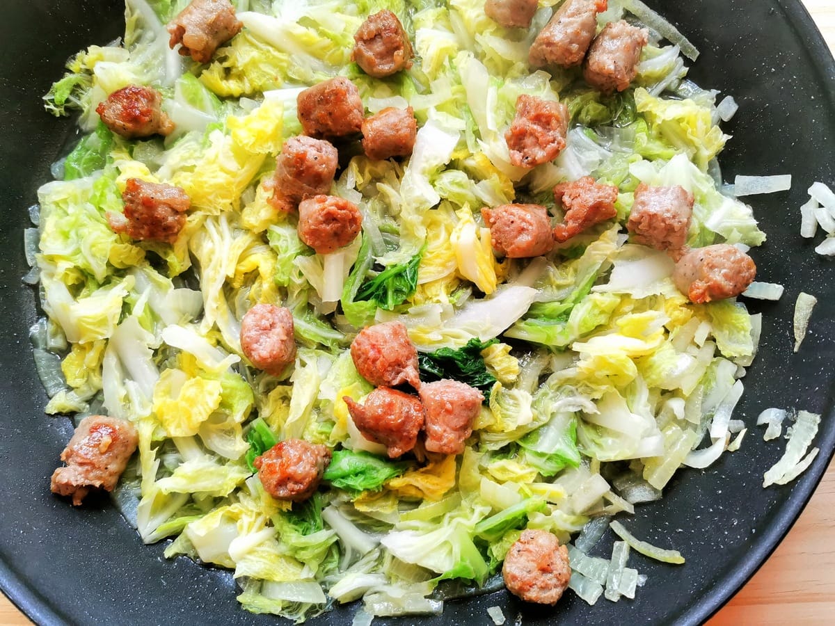 Cooked cabbage and pieces of sausage in frying pan.
