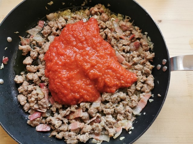 tomato passata added to skillet with sausage, guanciale and onion