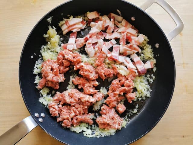 sausage meat, onions and guanciale cooking in skillet