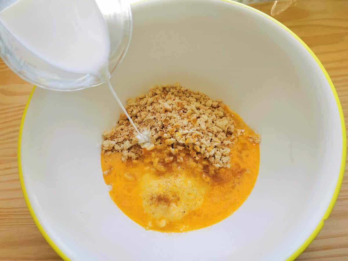Grated cheese, melted butter, breadcrumbs, spices and eggs in large bowl with milk being poured in.