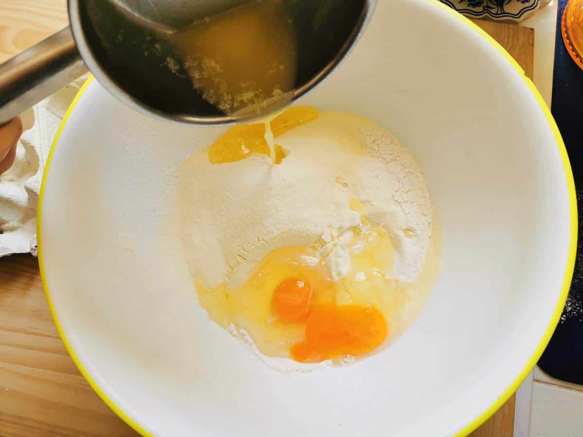 Flour and eggs in large bowl with melted butter being poured in.