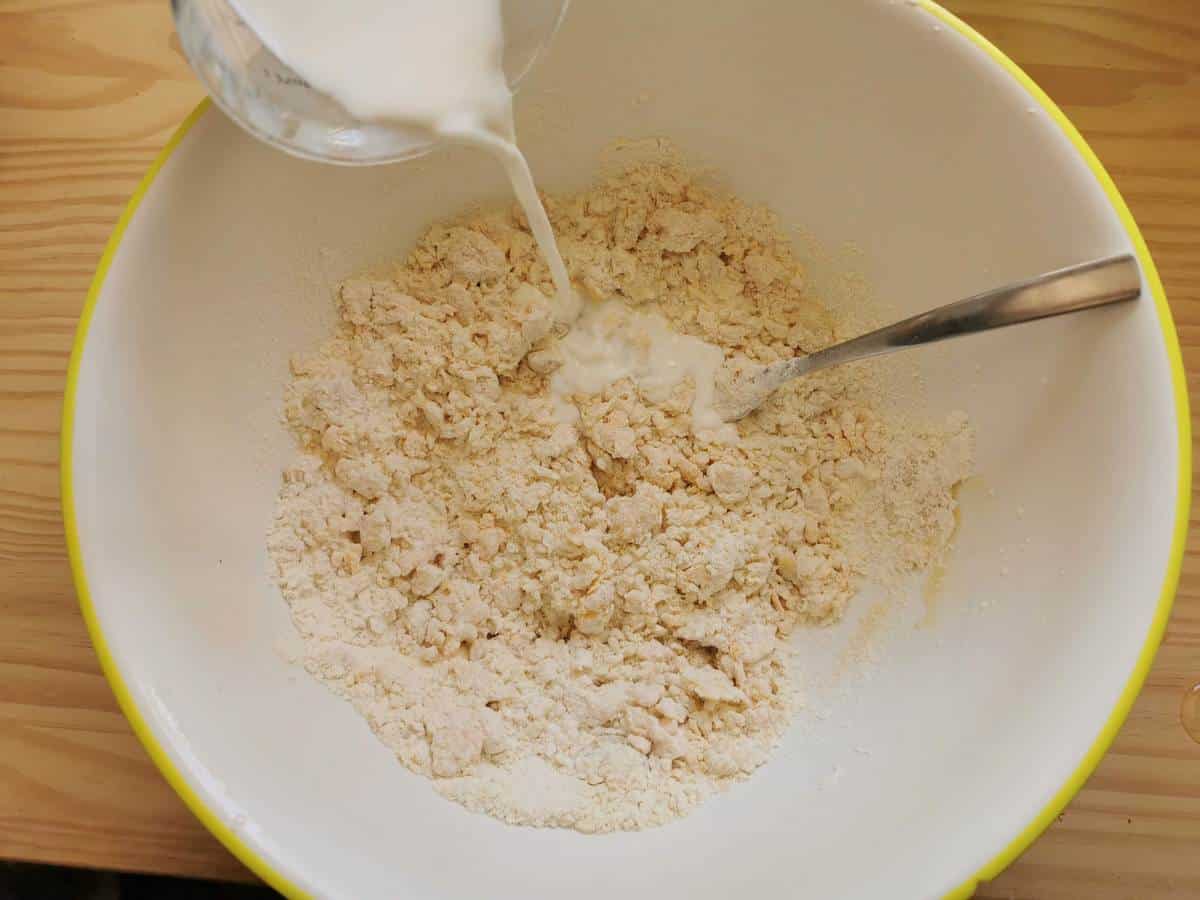 Mixed flour, eggs and butter in large bowl with milk being poured in.