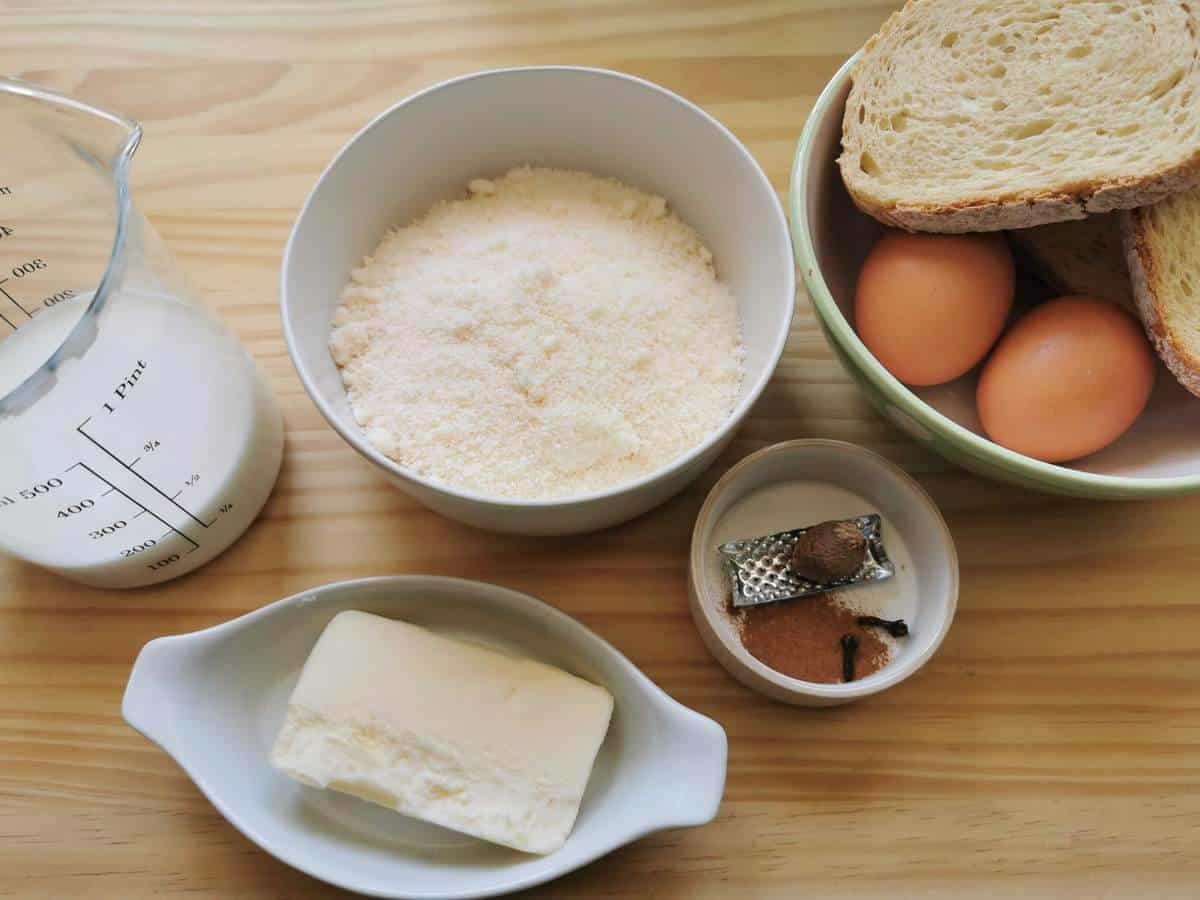 Ingredients for scarpinocc filling on wood work surface; milk, grated cheese, butter, eggs, stale bread and spices.