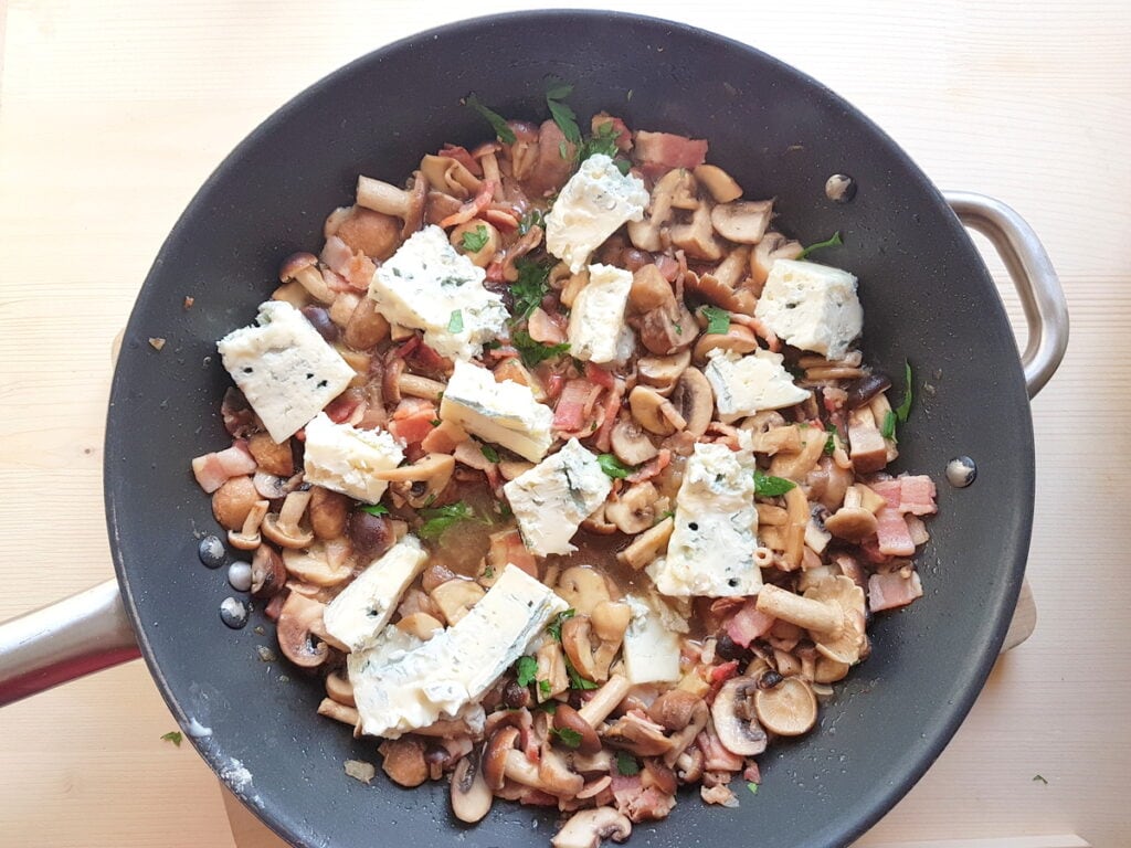 Pieces of gorgonzola in skillet with pancetta, onions and mushrooms