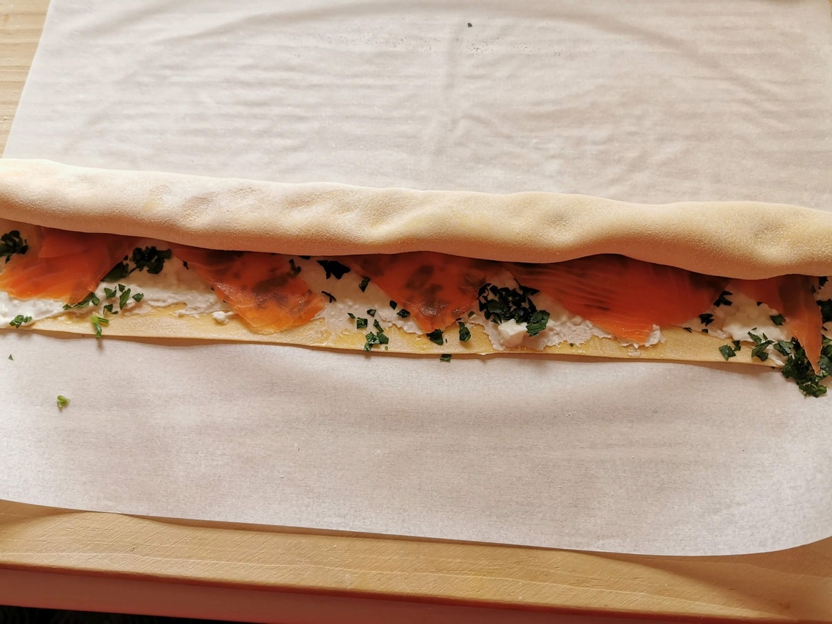 Pasta sheet with smoked salmon filling being rolled like a Swiss roll.