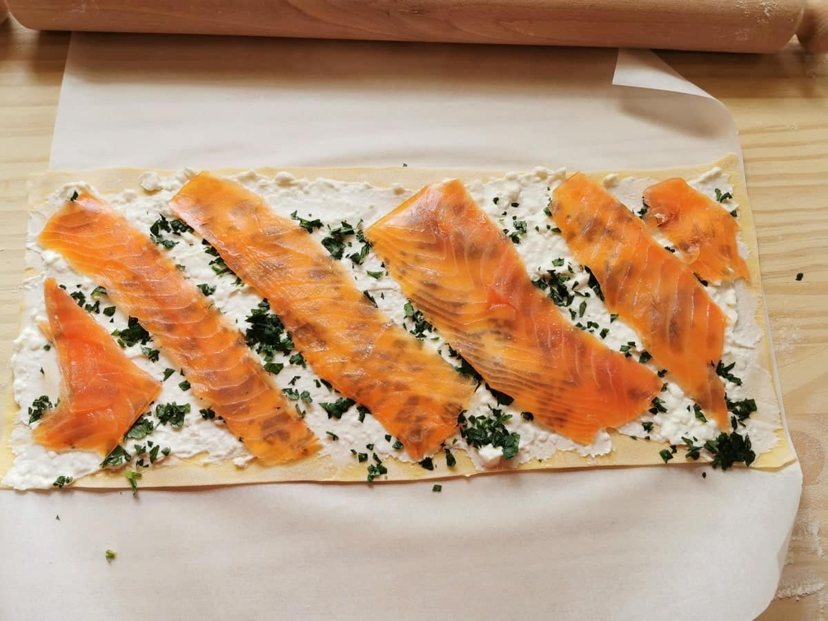 Slices of smoked sockeye salmon on pasta sheet with cheese and parsley.