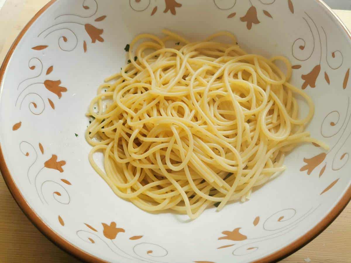 cooked spaghetti added to the colatura condiment in a large white bowl